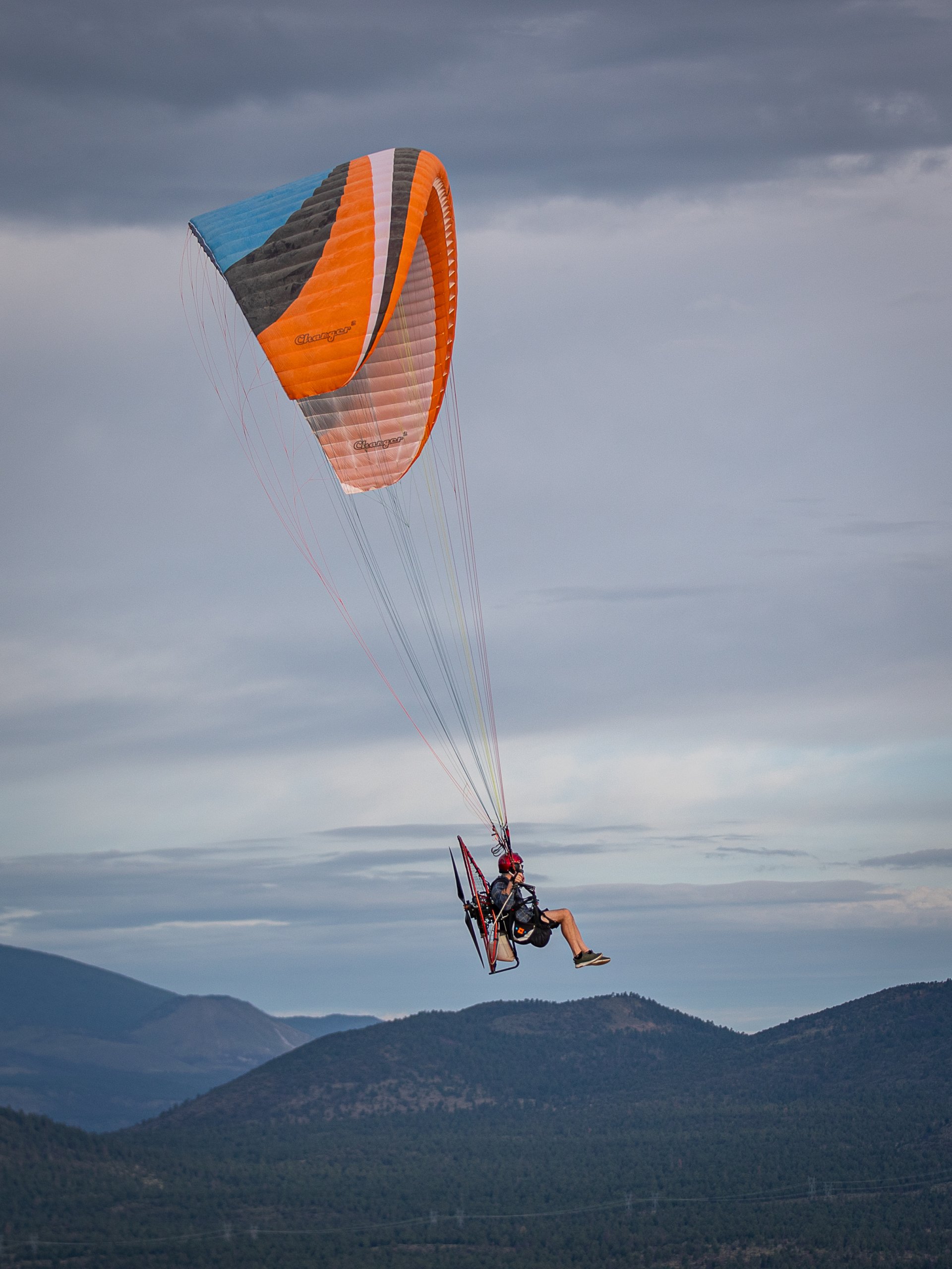 Pilot flying an orange wing above the mountains
